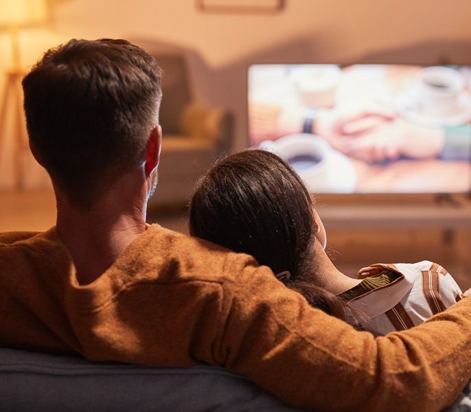 Family watching TV programming from their living room couch, viewed from behind