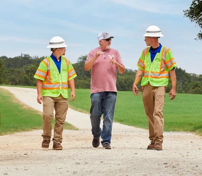 Spectrum technicians walking with a small business customer on a dirt road in a rural location